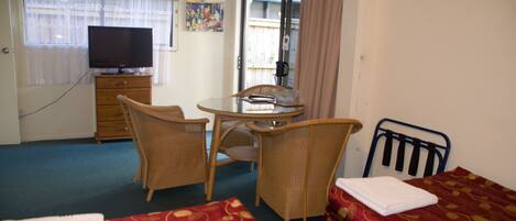 A hotel room with two beds, a television, a dining table with chairs, and a window with curtains.