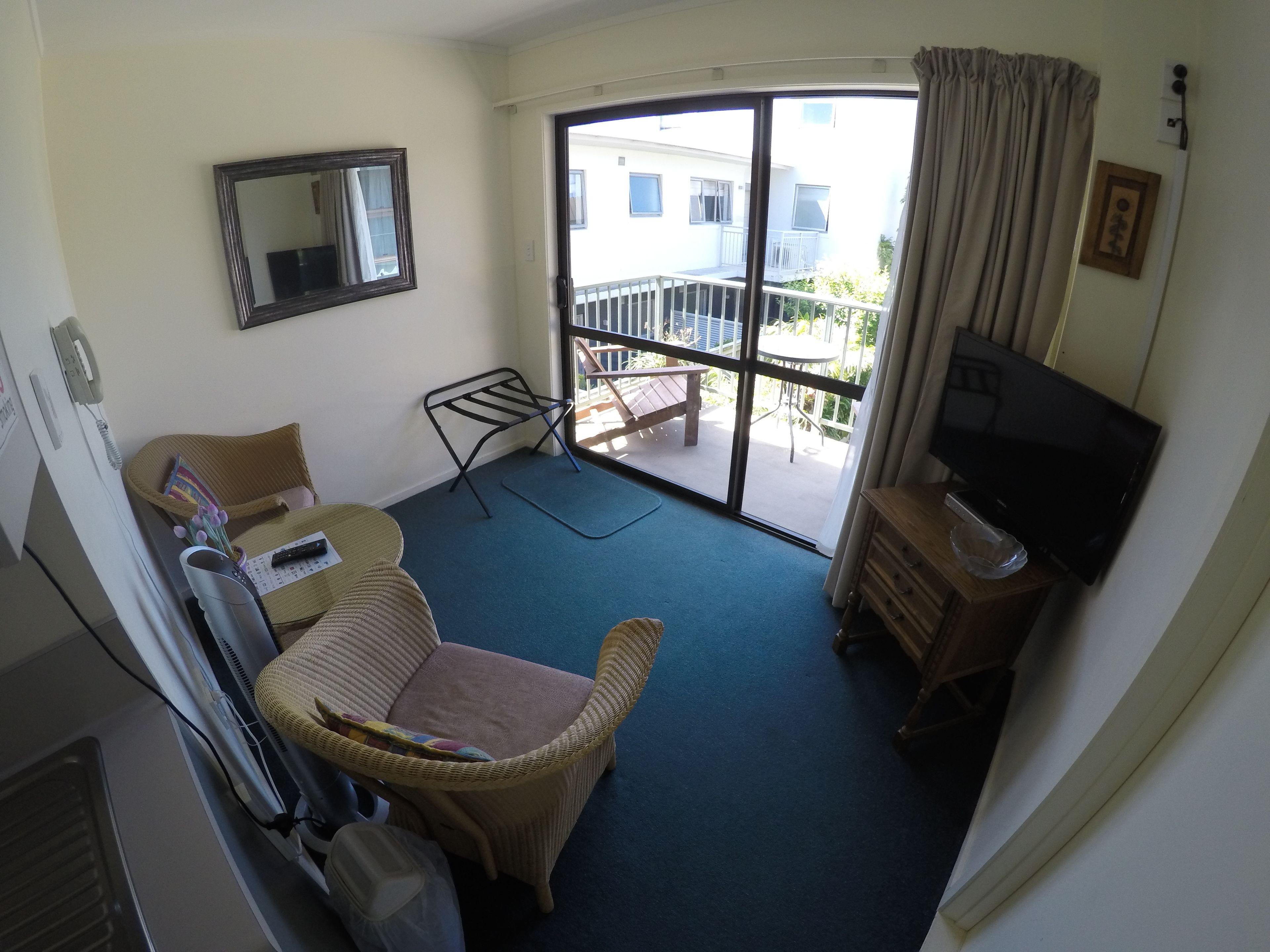 Een kamer met een rieten stoel, een tafeltje, een televisie en een balkon met een tafel en stoelen.