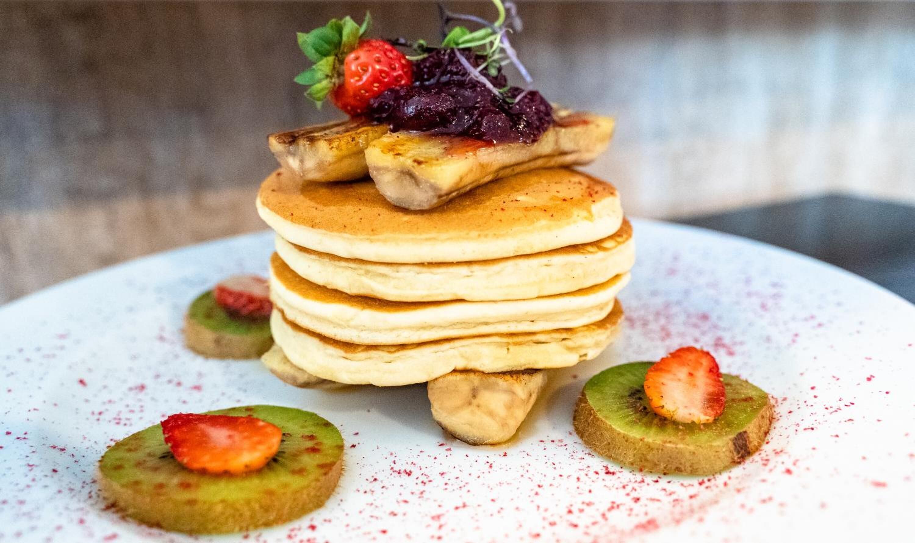 Een stapel pannenkoeken met aardbeien en kiwischijfjes op een wit bord.