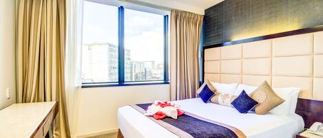 A hotel room with a large bed, a desk, and a view of the city.