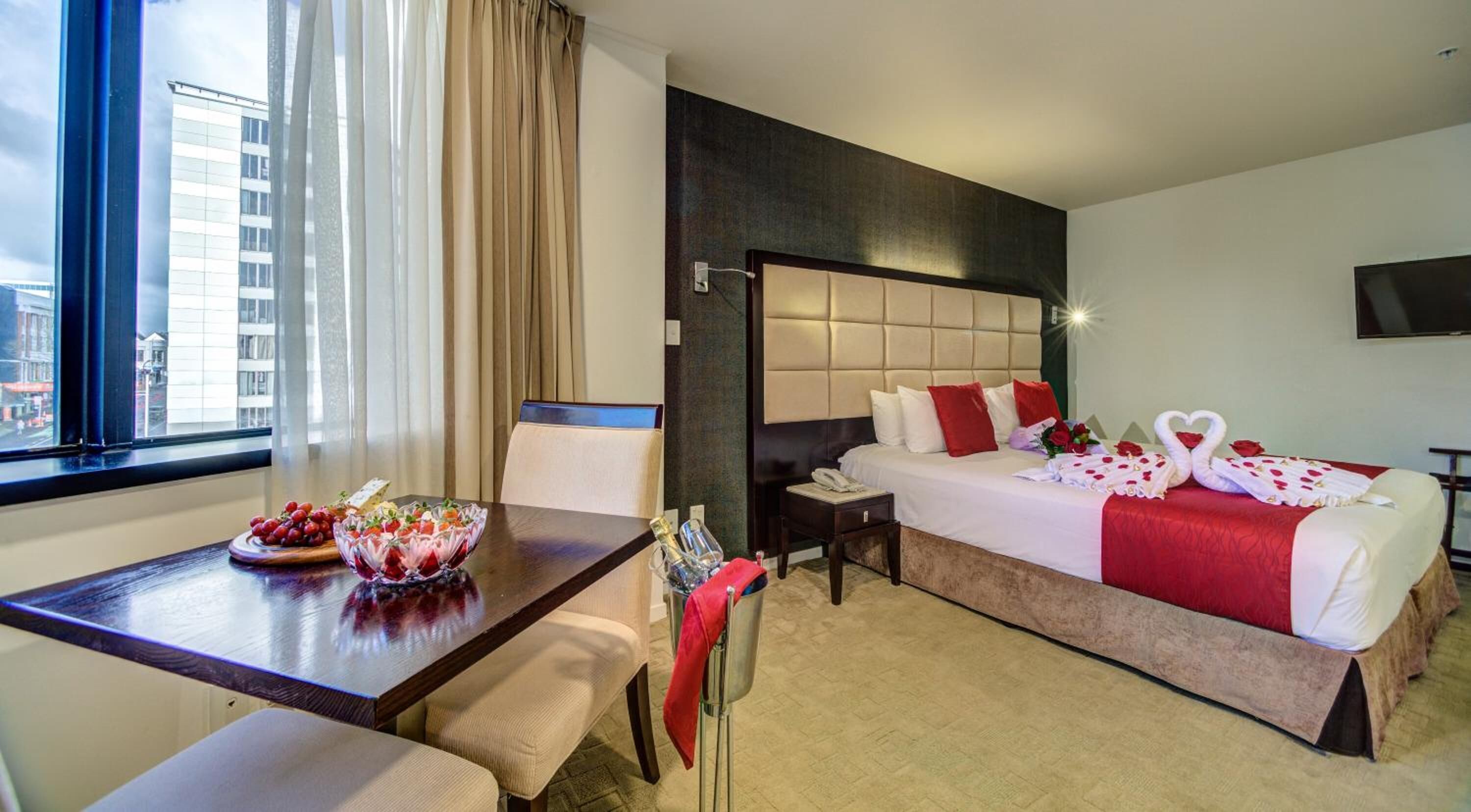 A hotel room with a bed, a desk with a bowl of fruit, a chair, a nightstand, and a TV.