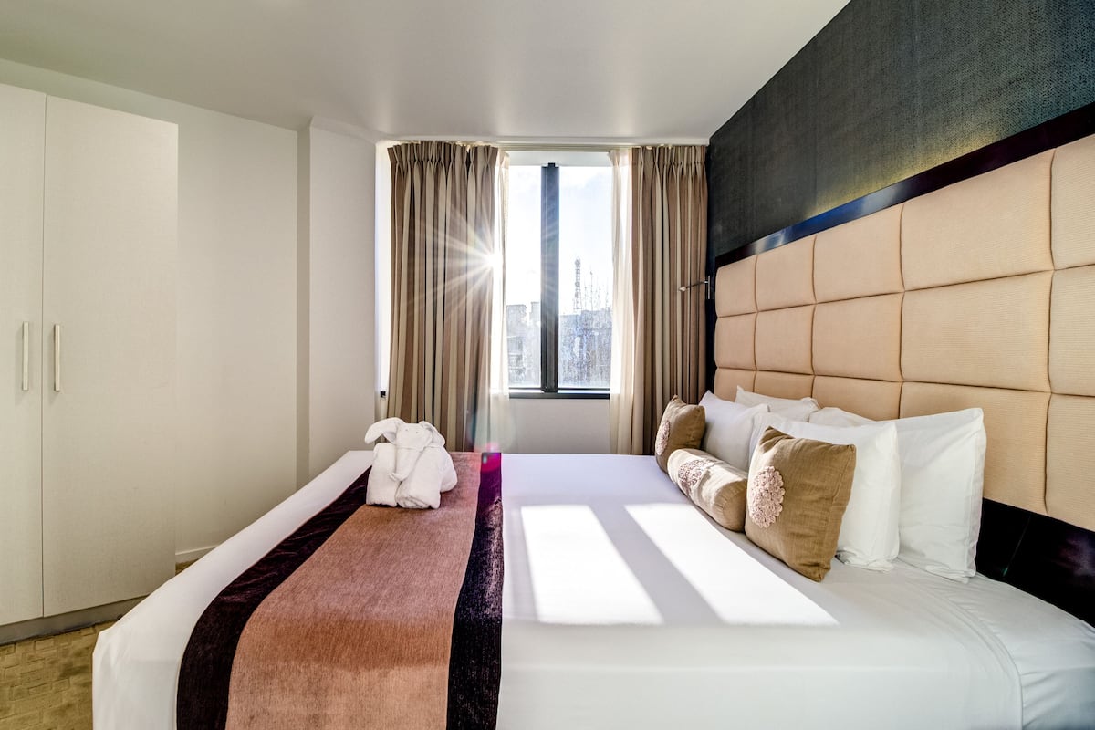 A hotel room with a large bed, a window with curtains, a city view, and a headboard with a tufted design.