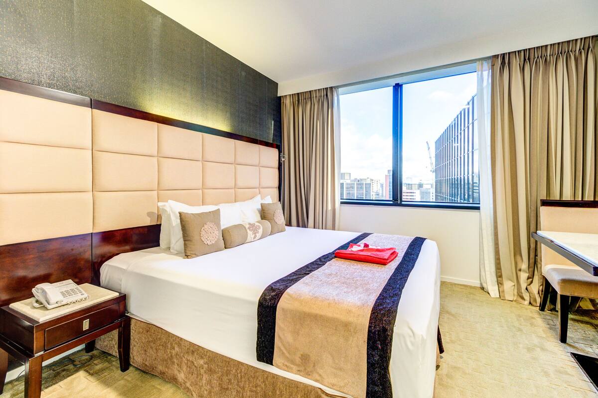 A hotel room with a large bed, a desk, and a window with curtains.