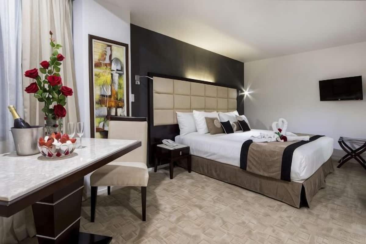 A hotel room with a bed, bedside table, chair, desk, and a TV mounted on the wall.