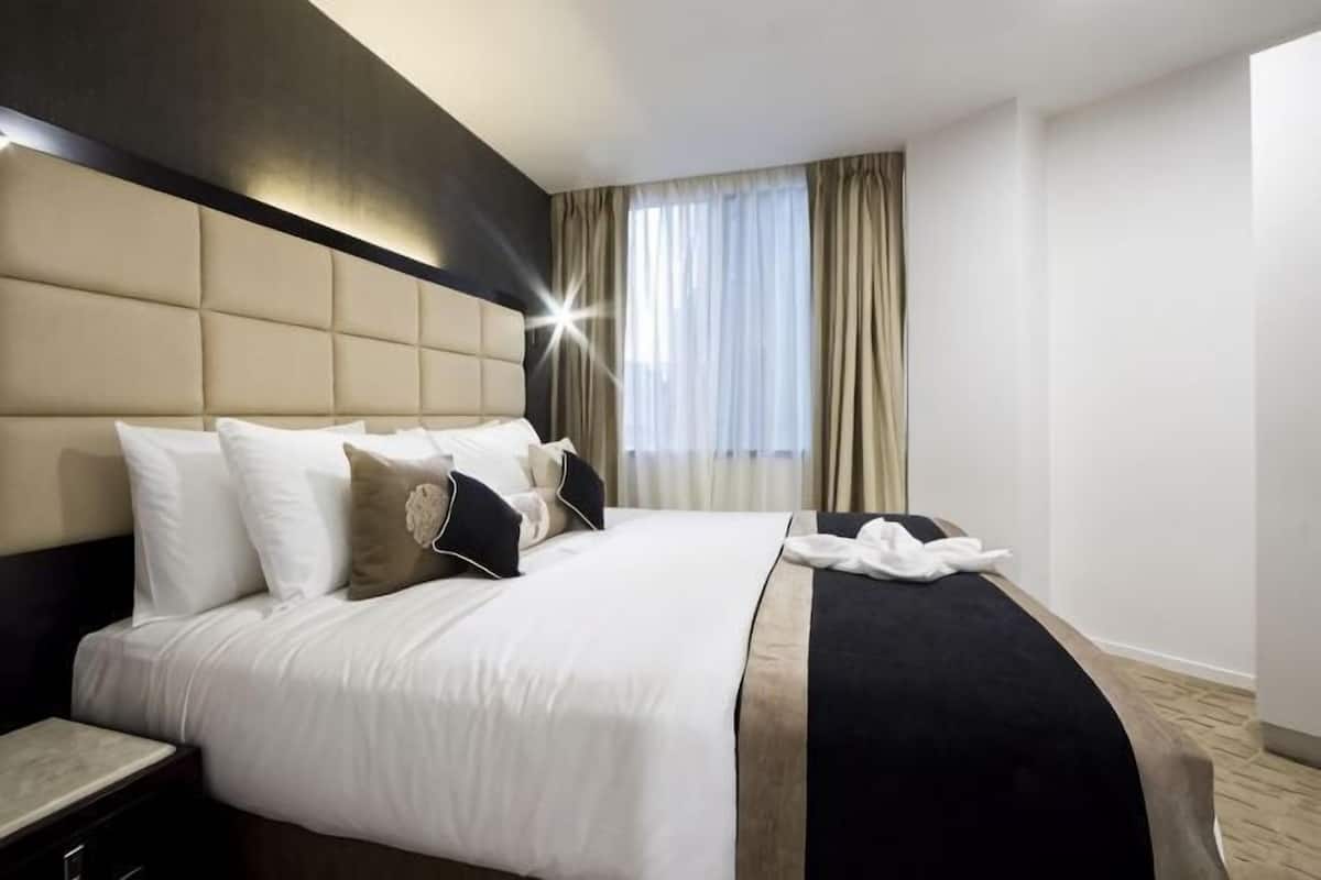 A hotel room with a large bed, a nightstand, a headboard, and a window with curtains.