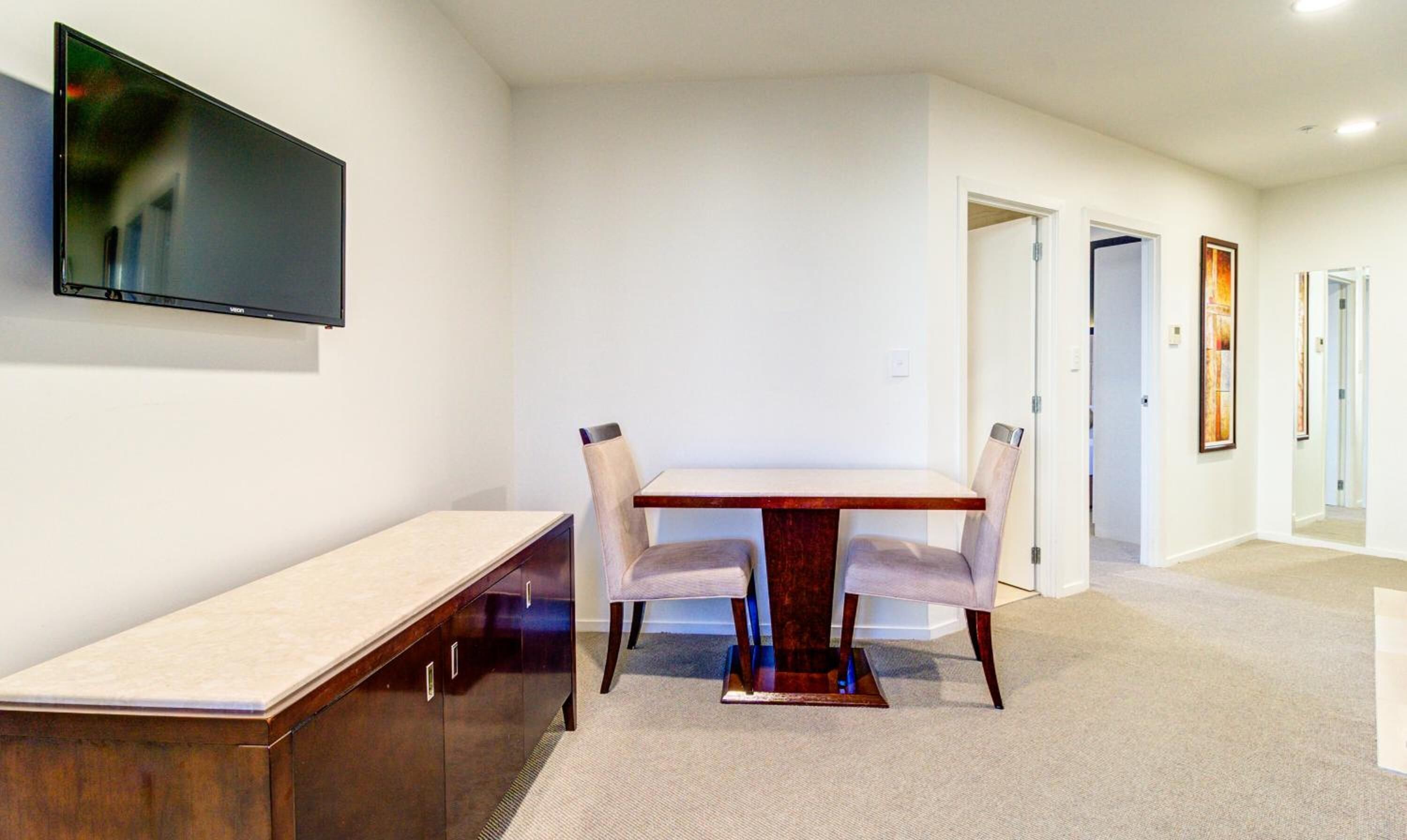 A modern dining area with a wooden table and chairs, a bench, and a flat-screen TV mounted on the wall.