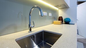 A modern kitchen with a stainless steel sink, a sleek faucet, and a countertop with a speckled pattern. - VR Queen Street - Hotel & Suites (Auckland)