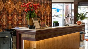 A reception desk with a vase of red tulips, framed certificates, and a small potted plant. - VR Queen Street - Hotel & Suites (Auckland)