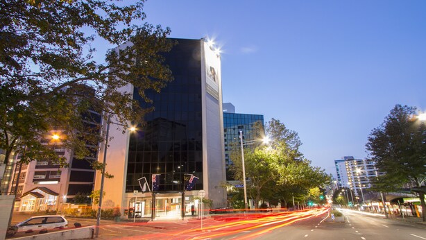 A modern building with a glass facade, a prominent vertical structure, and a street with light trails indicating traffic. - VR Queen Street - Hotel & Suites (Auckland)