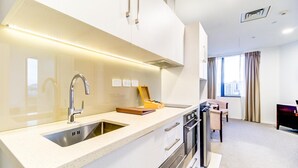 A modern kitchen with a stainless steel sink, a wooden box, and a dining area with a chair and table. - VR Queen Street - Hotel & Suites (Auckland)