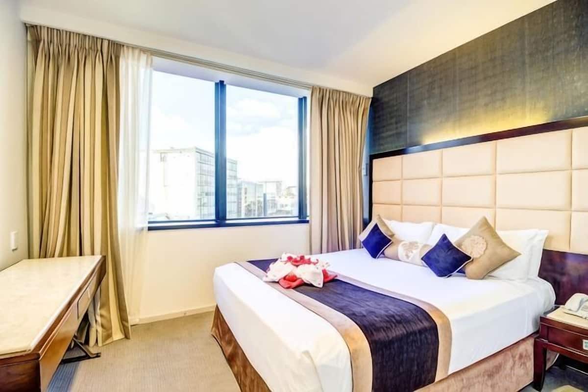 A hotel room with a bed, a desk, a window with curtains, and a city view.