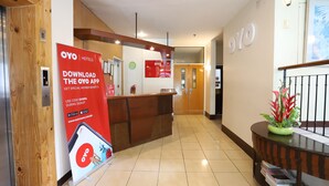 A hotel reception area with a wooden reception desk, a digital clock, and a sign promoting the OYO app.