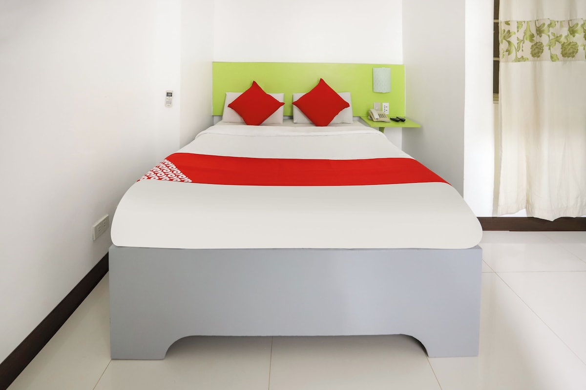 Una cama con una colcha blanca y roja, dos almohadas rojas y un cabecero verde.
