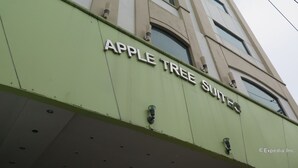 The exterior of the Apple Tree Suites building with a green facade and multiple windows.