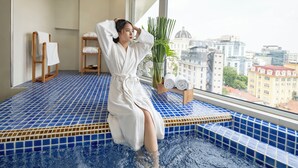 Una persona con bata blanca sentada en una bañera con azulejos azules y vistas a la ciudad.