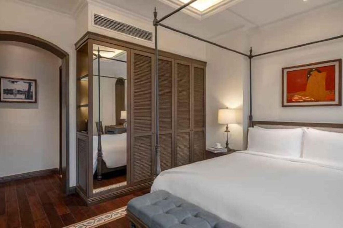 A hotel room with a large bed, a wardrobe, a mirror, a bedside table, and a painting on the wall.