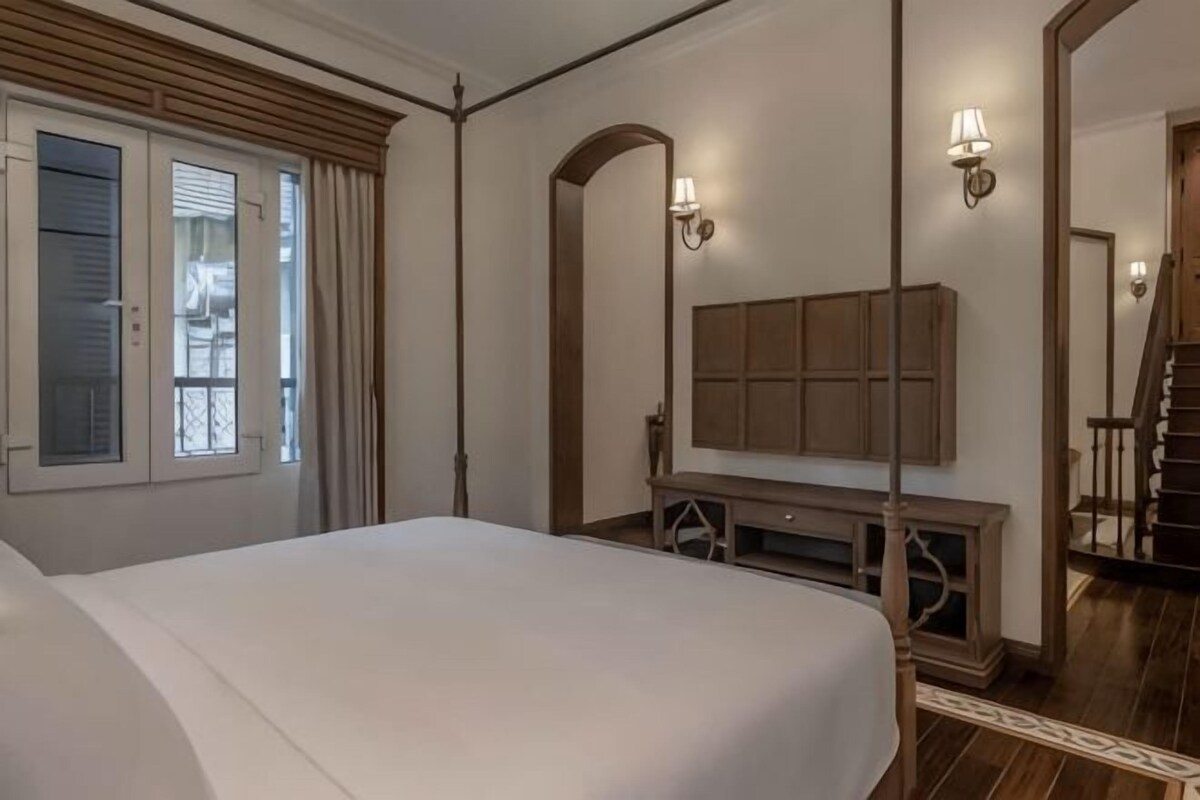 A bedroom with a bed, a wooden dresser, a mirror, and a window with curtains.