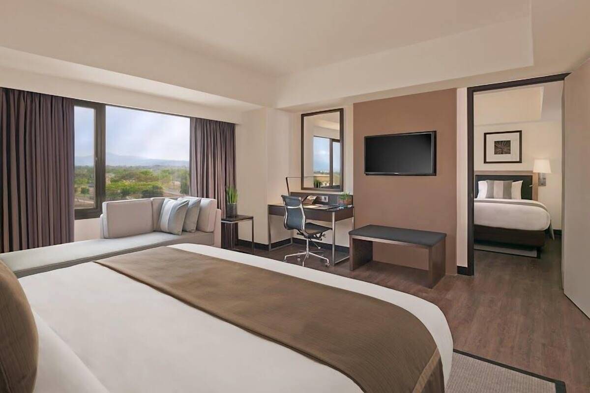A hotel room with a large bed, a desk, a chair, a TV, and a window with a view.