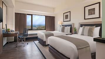 Habitación de hotel con dos camas, un escritorio, una silla, un televisor y ventanas amplias con vistas.