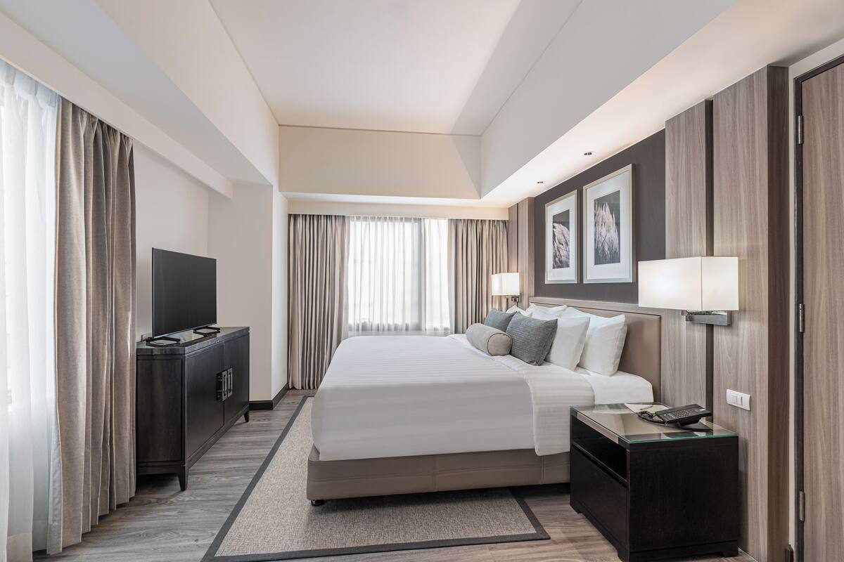 A modern hotel room with a large bed, bedside tables, a flat-screen TV, and a wardrobe.