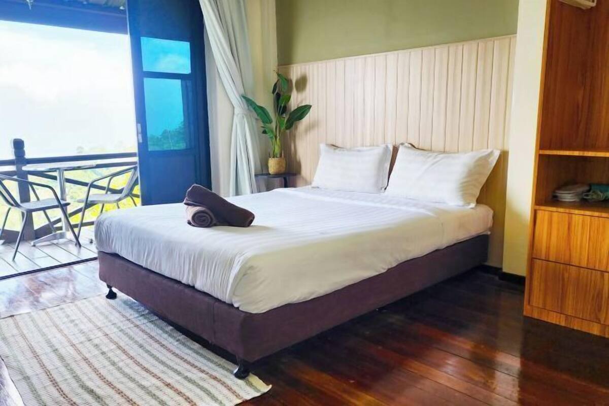 Un dormitorio con cama, cabecera de madera, una planta y vistas a través de un umbral abierto.