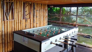 Une table de baby-foot dans une pièce aux murs en bambou, avec vue sur les arbres par une fenêtre.