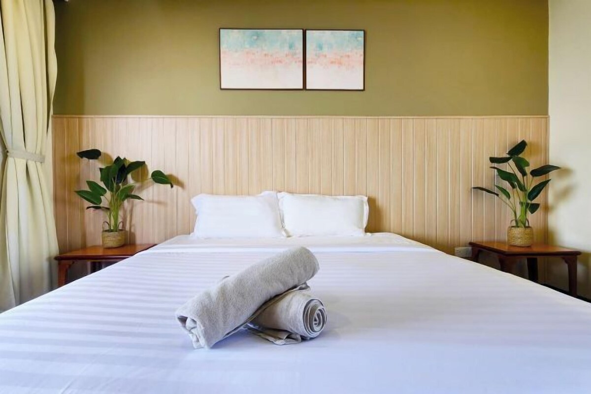 Une chambre d’hôtel avec un grand lit, deux tables de chevet ornées de plantes, une tête de lit et deux tableaux accrochés au mur.