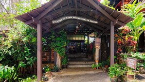 Une entrée traditionnelle en bois, surmontée d’un auvent, avec une pancarte indiquant : « Bienvenue au centre de bien-être Kasih Sayang. »