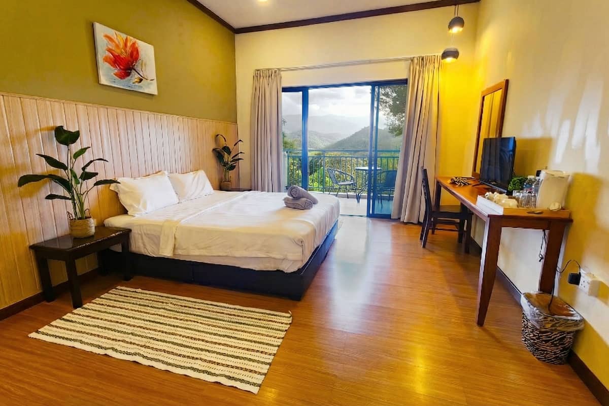 Un dormitorio con cama, escritorio, silla, planta en maceta y vistas al exterior.