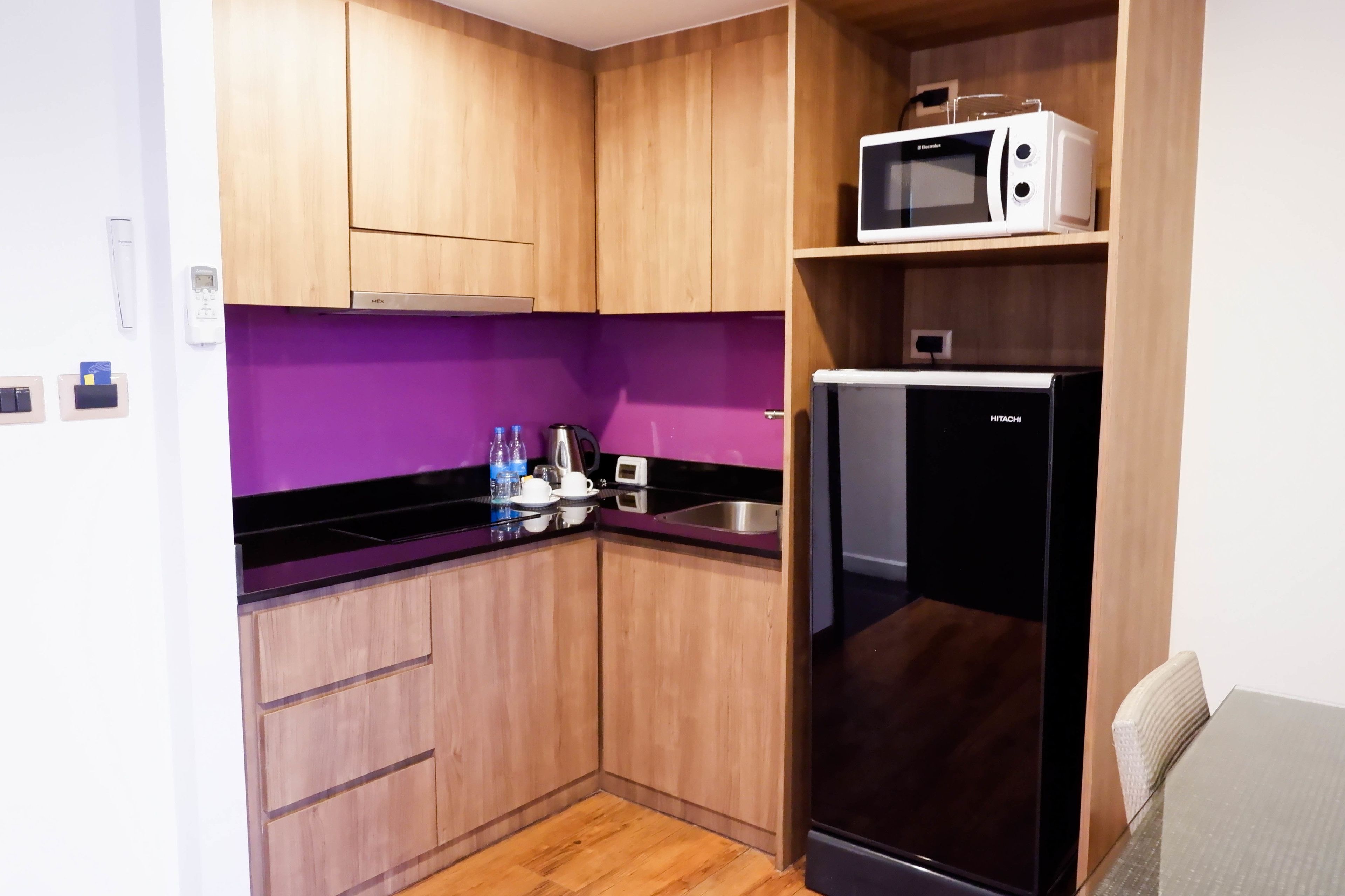 Una cocina compacta con armarios de madera, un refrigerador negro, un microondas y un salpicadero morado.