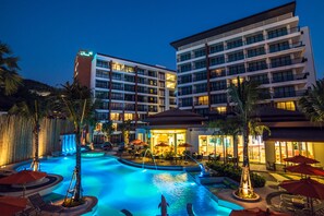 Un hotel con piscina, mobiliario exterior e iluminación destacada en la fachada.