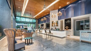 A modern lobby with a reception desk, seating area, and a large screen displaying a tropical scene. - The Beach Heights Resort (Karon)