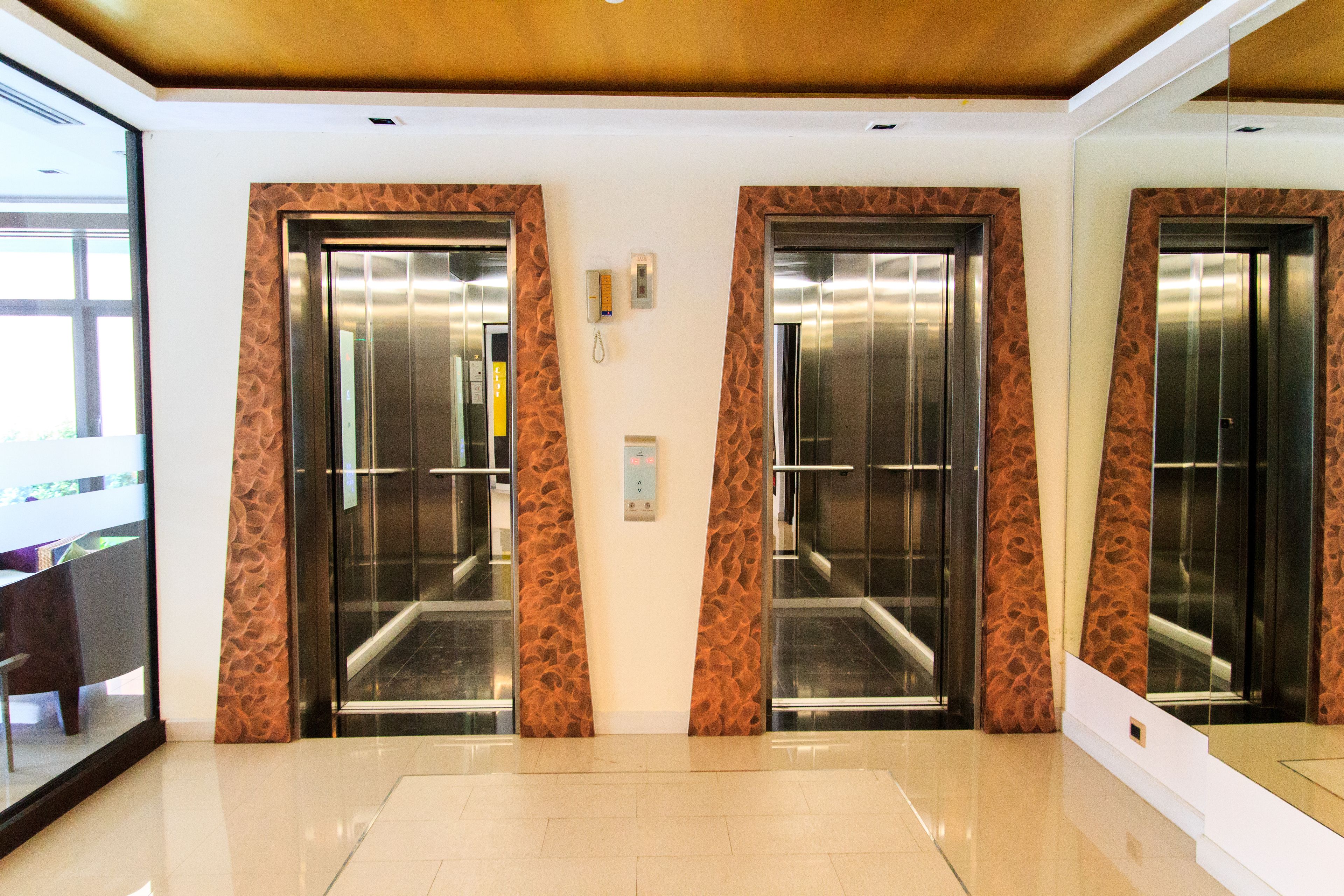 A modern elevator area with three elevators, each with a metallic finish and a patterned wall design.