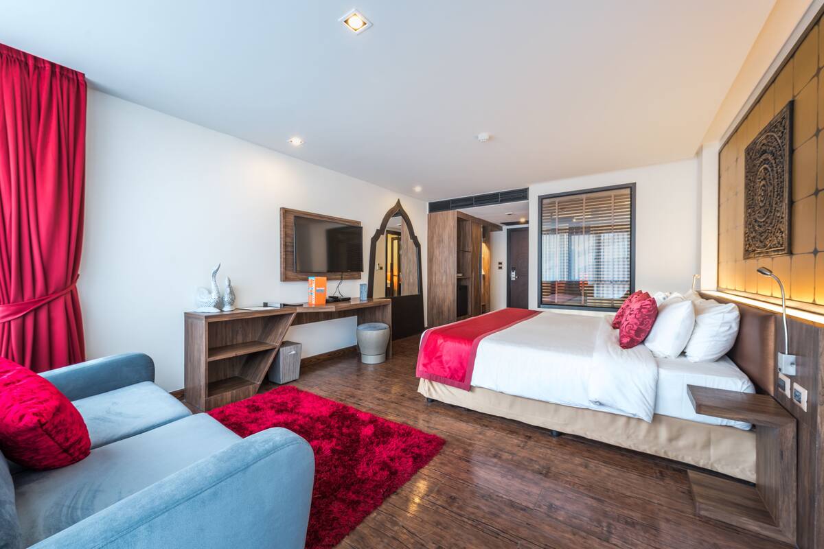 Una habitación de hotel moderna con cama, escritorio, silla, alfombra roja y un espejo grande.