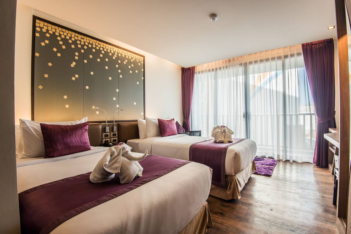 Habitación de hotel con dos camas, un panel de pared grande con patrones geométricos y un ventanal con cortinas de gasa.