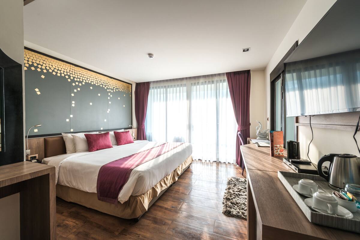 Habitación de hotel moderna con una cama grande, piso de madera, un escritorio con hervidor y vistas al exterior.