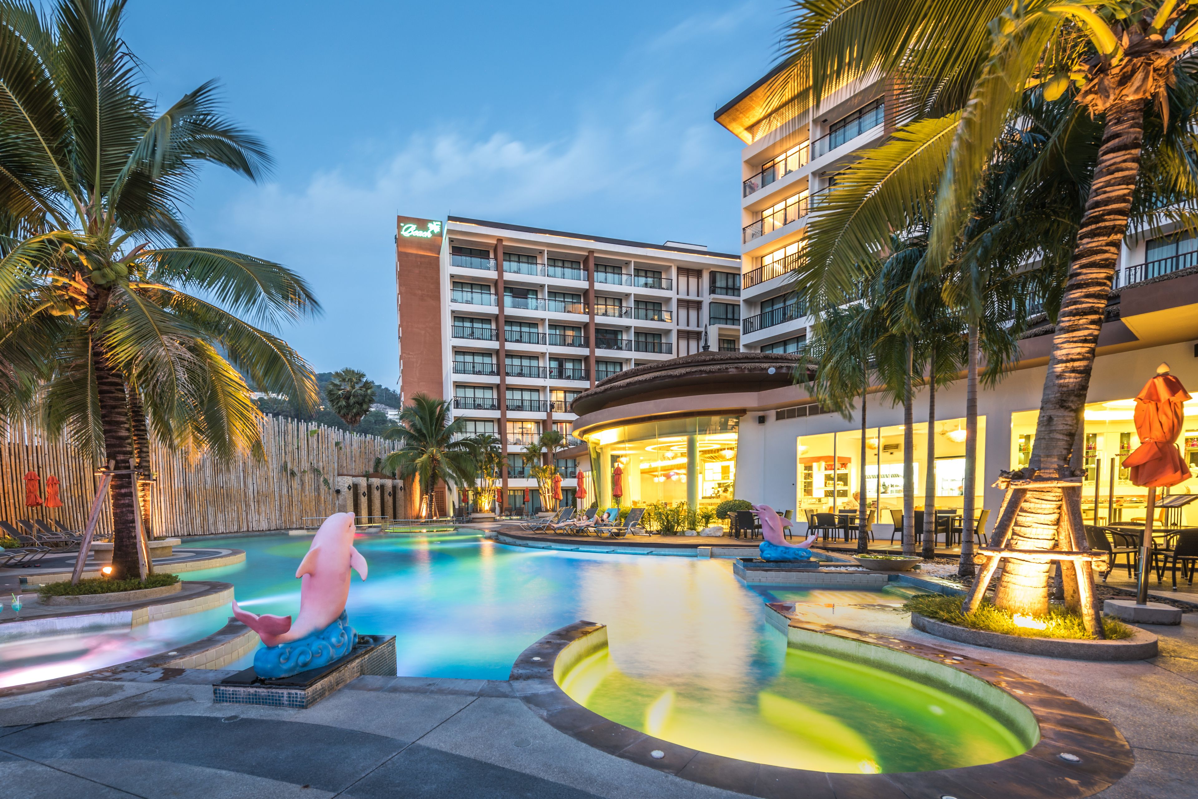 A hotel with a swimming pool, palm trees, and a building with multiple floors and balconies.
