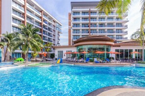 Un hotel con piscina, palmeras y zonas de estar al aire libre.