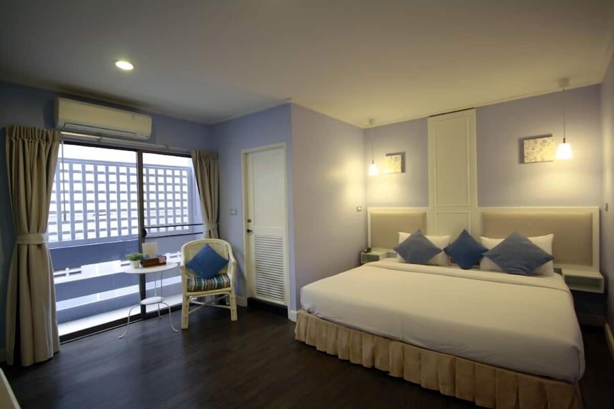 A hotel room with a large bed, a chair, a small table, and a window with curtains.