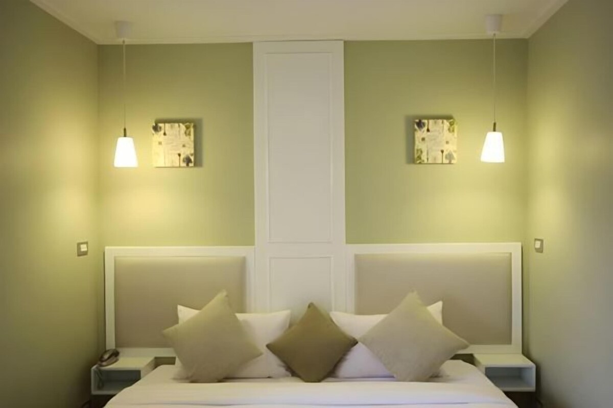 Una habitación de hotel con cama, mesitas de noche y dos lámparas fijadas a la pared.