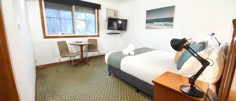 A hotel room with a bed, a desk, two chairs, a TV, and a window with a view.