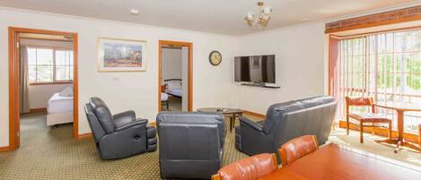 A spacious living room with a wooden dining table, leather sofas, and a TV mounted on the wall.