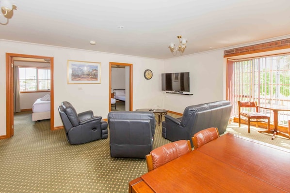 A spacious living room with a wooden dining table, leather sofas, and a TV mounted on the wall.
