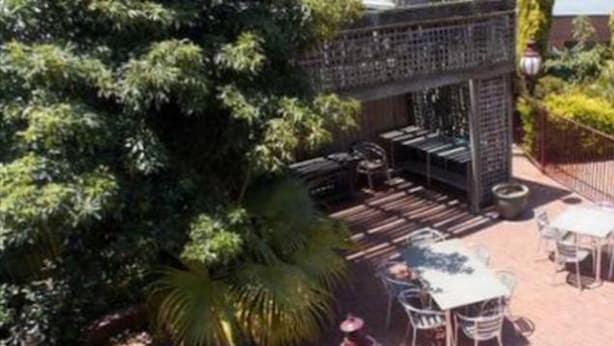 Un patio al aire libre con mesas y sillas, rodeado de abundante vegetación y un farol decorativo.