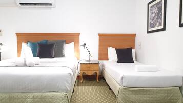 A hotel room with two beds, a nightstand, a lamp, an air conditioner, and a framed picture on the wall.
