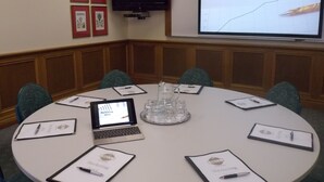 Un salón de conferencias con una mesa redonda, portátiles y pantallas de presentación que muestran 'Marketing 2013'.