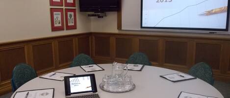 A conference room with a round table, laptops, and presentation screens displaying 'Marketing 2013'.