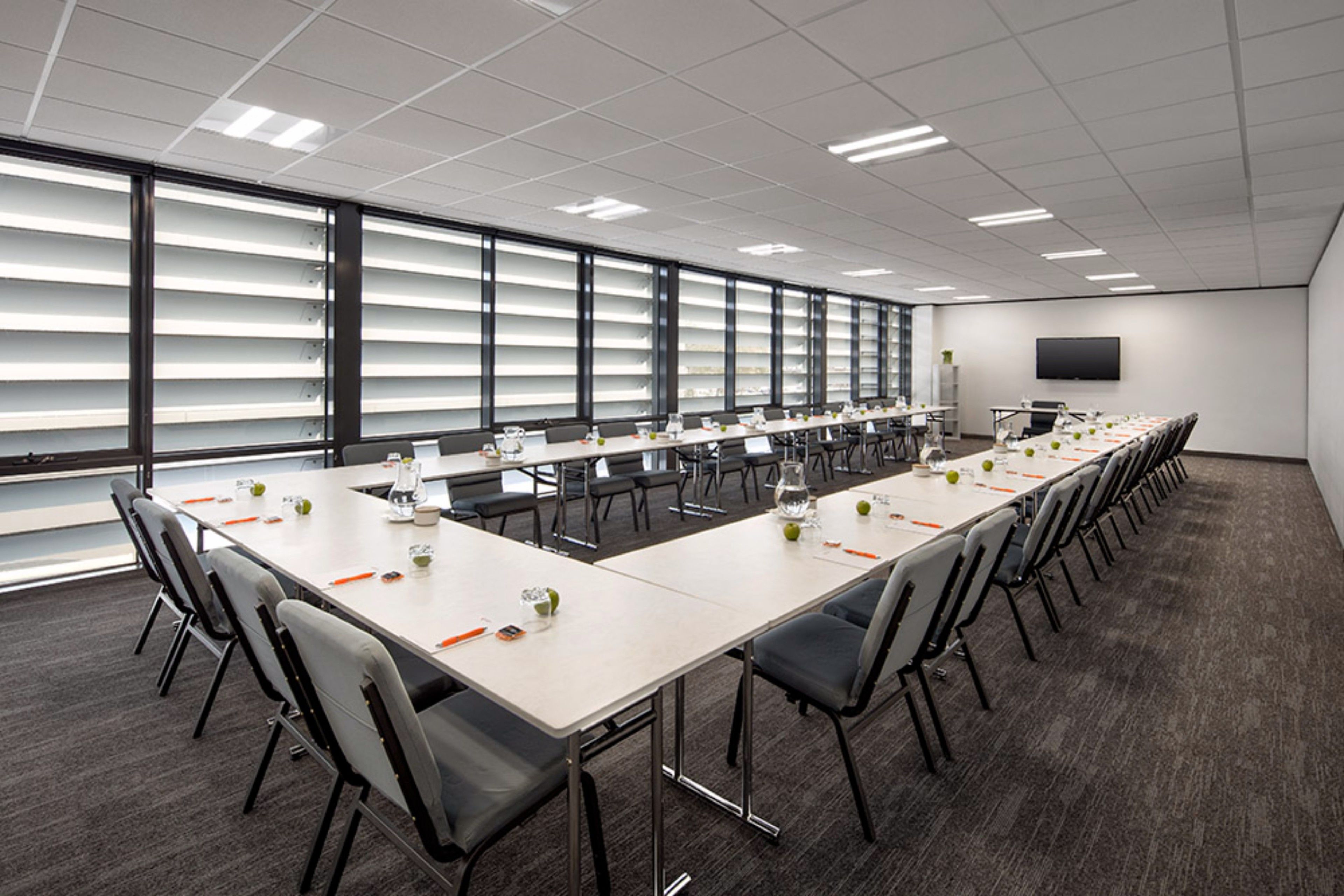 A conference room with a long table, chairs, and a TV on the wall.