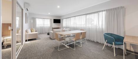 A modern hotel room with a large bed, a desk, a chair, and a dining table.