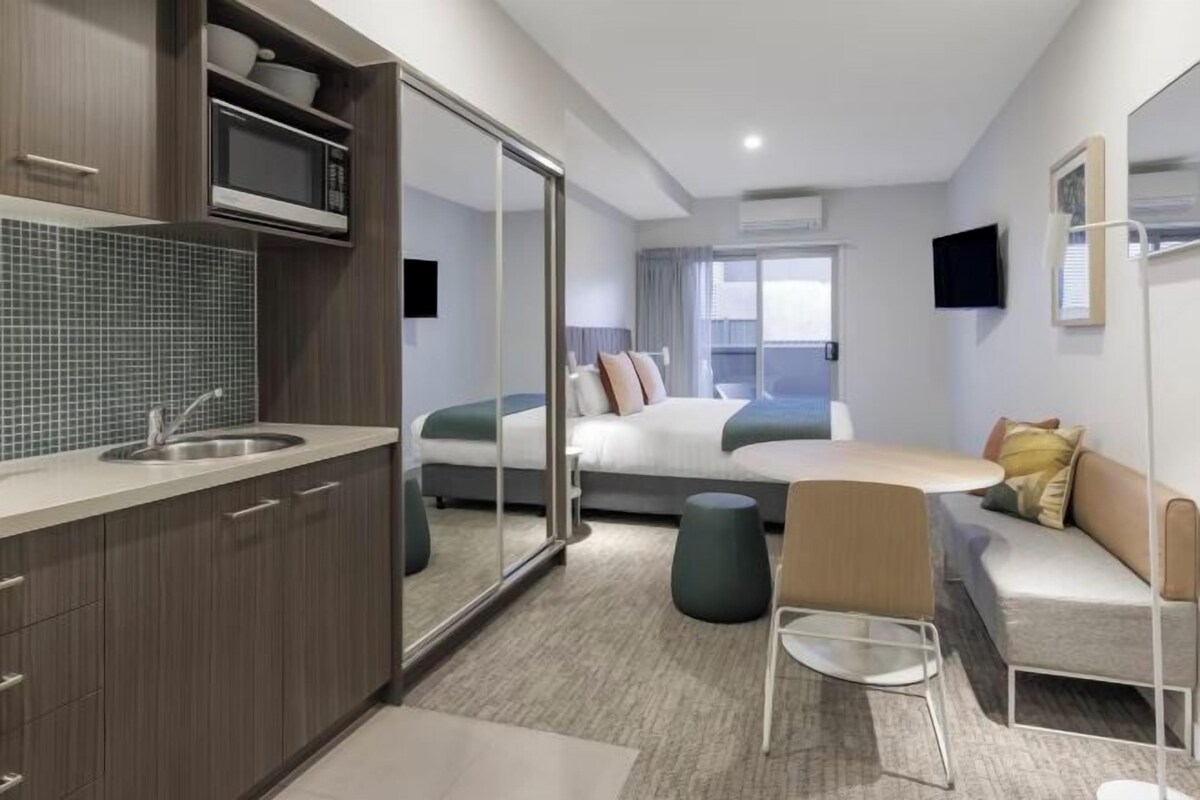 Una habitación de hotel moderna con kitchenette, una cama con vistas, un sofá y una mesa de comedor.